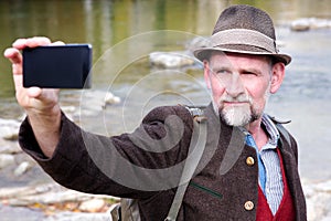 Bavarian man in his 50s standing by river and taking a selfie