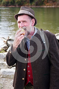 Bavarian man standing by river and eating apple