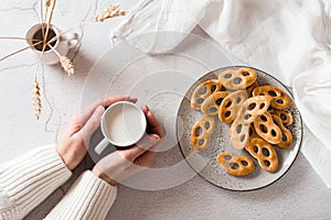 Bavarian pretzels on a plate and a cup of milk in female hands on the table. Snack for fast food. Top view