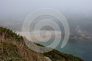 The bay, the beach with sand and blue water in heavy fog, people on the beach sunbathe from above from the mountain