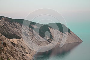 A bay with a beautiful sheer cliff at sunset with blue sea water. Rocks by the ocean, rocky ledge, cliff