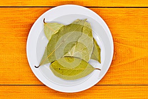 Bay leaf. Laurel tree leaves on a white plate on an orange wooden table. Culinary spices. Flavoring spices for cooking. Additives