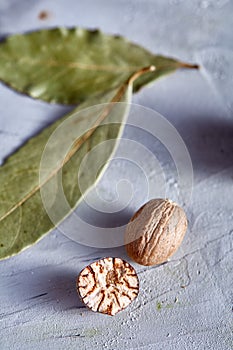 Bay leaf and nutmeg on white textured background, top view, close-up, selective focus, vertical.