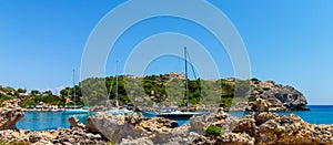 A bay in the Mediterranean with sailing ships and rocks in the foreground