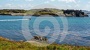 Bay with a motorboat sailing with the ruins of Cromwellâ€™s Barracks in the background on Inishbofin Island