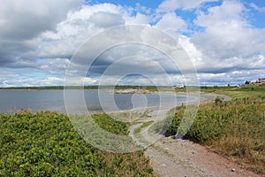 A bay with a rocky gravel beach surrounded by fields and forests on Isle Madame.