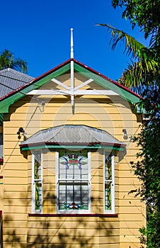 Bay window on yellow traditional Australian Queenslander House with tin roof and tropical trees