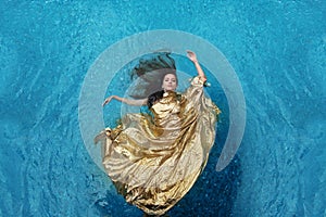 Bbeautiful young woman in gold dress, evening dress floating weightlessly elegant floating in the water in the pool