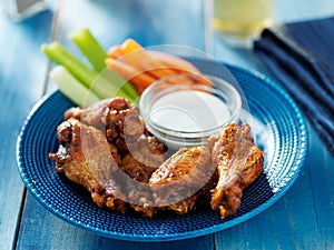 Bbq buffalo chicken wings on blue plate with ranch dip and celery sticks