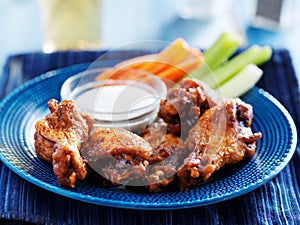 Bbq buffalo chicken wings on blue plate with ranch dip and celery sticks