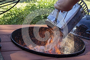 Bbq chimney charcoal fire starter full of burning briquettes being dumped into an outdoor grill with sparks flying