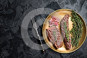 BBQ grilled Bavette Bavet beef meat steak with herbs on a plate. Black background. Top view. Copy space