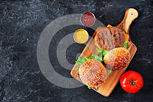 BBQ hamburgers on a serving board, top view over a slate background