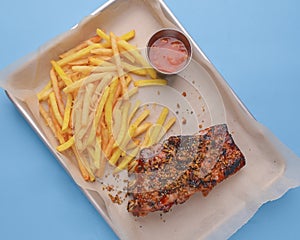 BBQ marinated spareribs and french fries with sauce. Barbecue cooked ribs with spice and sauce served on a metal tray