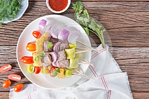 Bbq meat on sticks, kebab skewers with vegetable sticks and tomato sauce on wooden background.