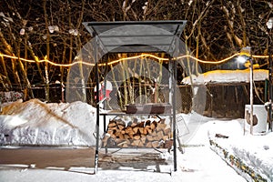 BBQ near the home in the winter. Night, garlands are burning, it is snowing. Preparation for roasting meat. They lay harvested
