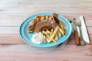 BBQ pork ribs, onion rings, french fries and coleslaw in blue plate on table