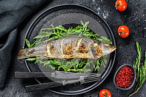 BBQ sea Bass fish with arugula, fried sea bass. Black background. Top view