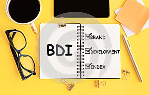 BDI - brand development index. Text on notepad and office accessories on yellow desk