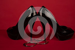 BDSM role play concept. Sexual behaviour. Shoe on high heel with handcuffs on red background.
