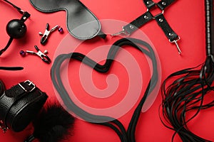 BDSM set on red background. BDSM accessories and rope in the shape of a heart. Mask, handcuffs, ball gag and a whip