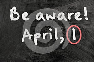 Be aware on blackboard note over a dark background. april fools day