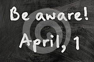 Be aware on blackboard note over a dark background. april fools day