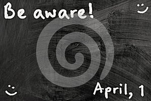 Be aware on blackboard note over a dark background. april fools day