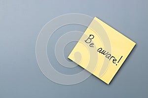 Be aware on yellow sticky note over a grey background. april fools day