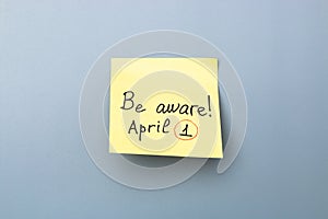 Be aware on yellow sticky note over a grey background. april fools day