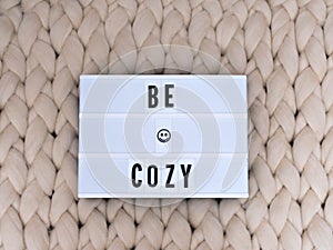 BE COZY word on lightbox on knit background. Cozy compozition. Knit background.