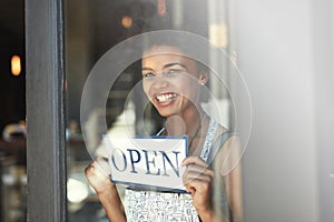 Be the first to join us for a delicious coffee. a young woman hanging up an open sign on the window of her cafe.