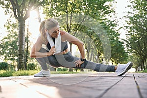 Be fit. Attractive middle aged athletic woman in sportswear with towel around her neck stretching her legs while