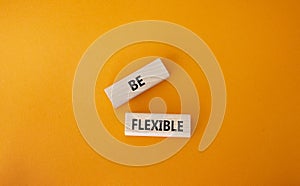 Be Flexible symbol. Wooden blocks with words Be Flexible. Businessman hand. Beautiful orange background. Business and Be Flexible