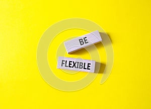 Be Flexible symbol. Wooden blocks with words Be Flexible. Businessman hand. Beautiful yellow background. Business and Be Flexible