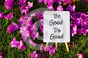 Be good do good. On background of pink flowers and green grass.