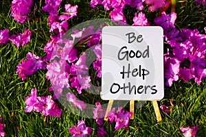 Be good help others. On background of pink flowers and green grass.