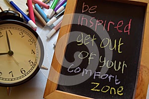 Be inspired get out of your comfort zone on phrase colorful handwritten on chalkboard, alarm clock