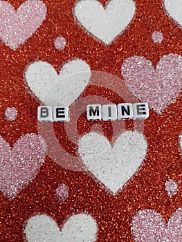 Be mine on a pink white and red sparkly background for valentine's day