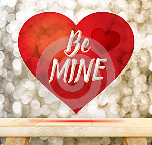 Be mine word in red heart floating above wood table at gold blur