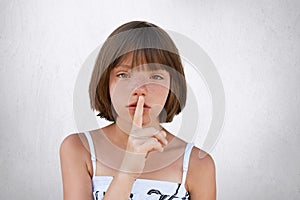 Be silent, hush! Adorable small kid showing silent sign asking to be noiseless as her little sister is sleeping. Freckled girl wit photo