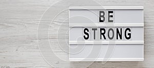 `Be strong` words on a lightbox on a white wooden background, top view. Overhead, from above, flat lay. Space for text