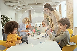 Be technology literate. Diverse children assembling and programming robots during STEM class with young female teacher