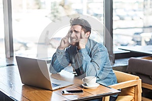 Be waiting an idea! Side view portrait of thoughtful bearded young freelancer in blue jeans shirt are sitting in cafe and working