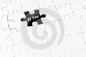Be you. White puzzle jigsaw with missing piece and text on black. Dare to be different concept. Be yourself. Self love care.