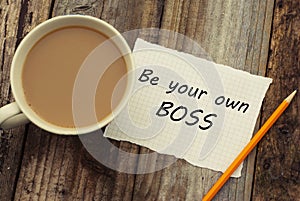 Be Your Own Boss motivational inscription on white paper, with cup of coffee over rustci wooden table.