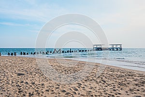 Beach with abandoned ruin pier over blue sea and sky