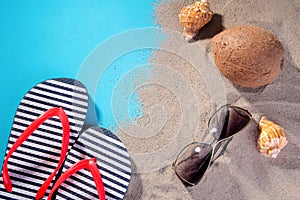 Beach accessories. Flip flops, glasses from the sun, shells and coconut on the sand of the sea. on a blue background.