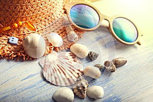 Beach accessories glasses hat cockleshells on wood deck.