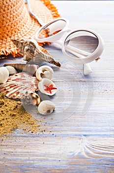 Beach accessories glasses hat cockleshells on wood deck.